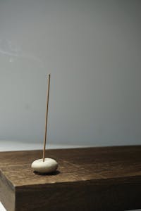 A simple incense stick releasing smoke on a wooden surface, creating a peaceful ambiance.