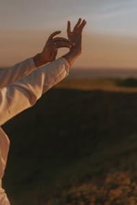 Hands reaching towards the sky during a peaceful sunset in a natural setting, embracing tranquility.