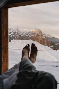 Peaceful winter morning with feet propped up, overlooking snowy mountains through a window.